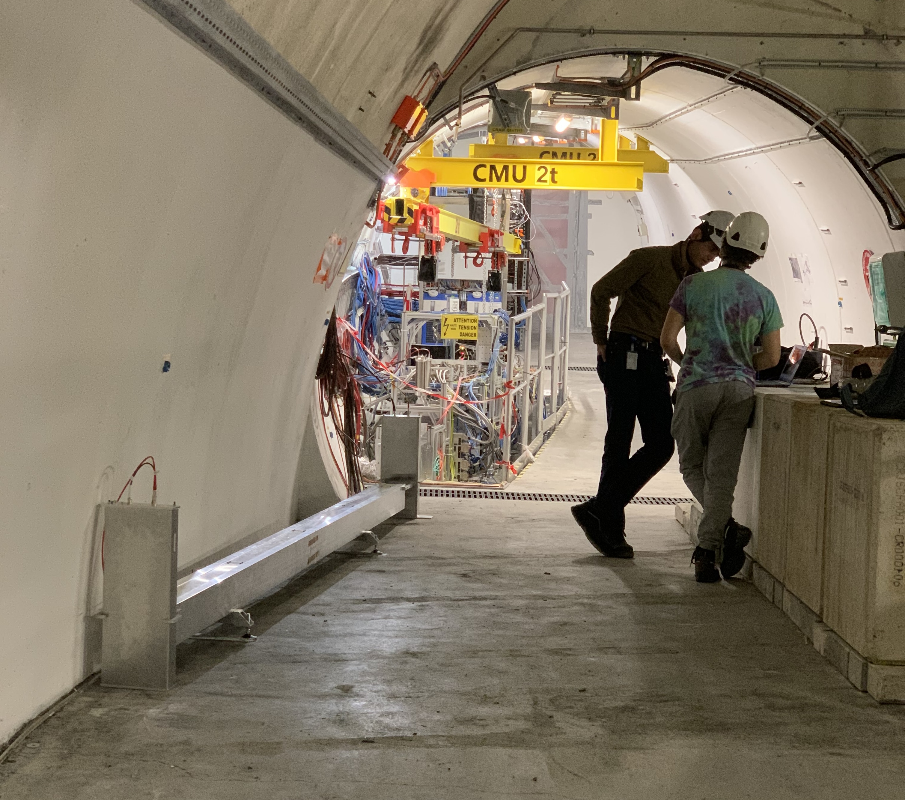 A small underground space, with the Formosa experiment (a long silver paraliped) on the left and two men chatting on the right. In the background is the FASER experiment installation.